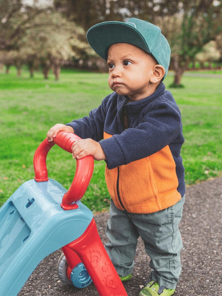 bebê utilizando um andador de empurrar para brincar no jardim