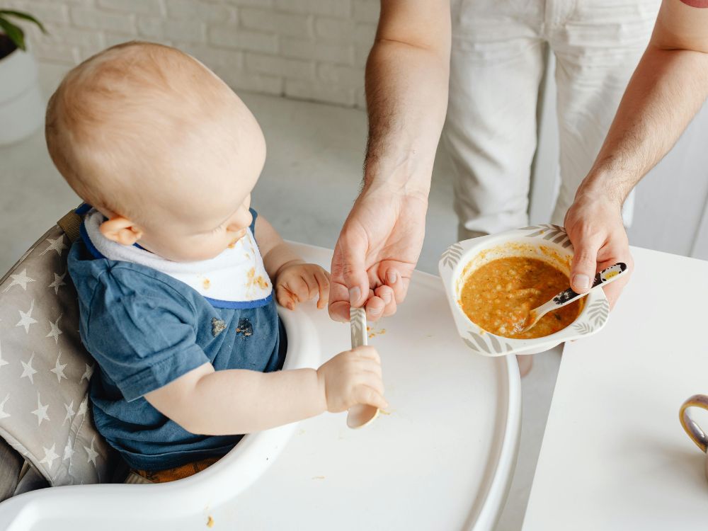 mãe dando ao bebê uma papinha laranja na introdução alimentar dele