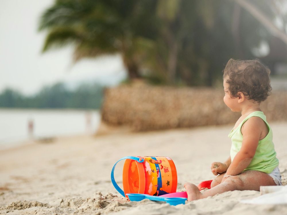 bebê brincando na praia. para proteger bebês e crianças no tempo seco, evite exposição ao sol