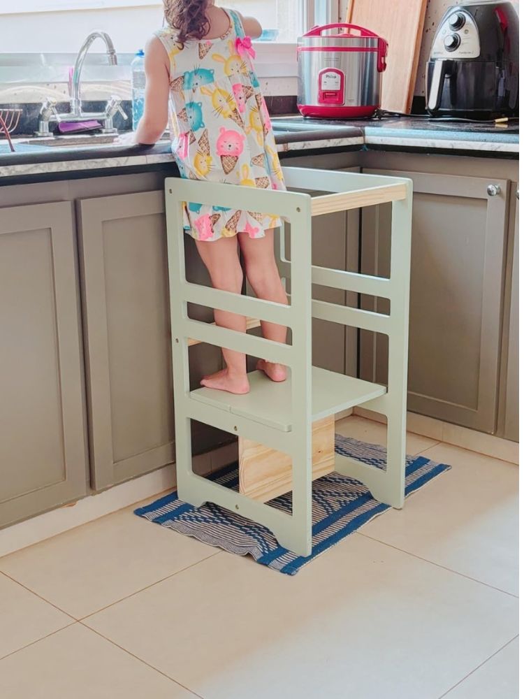 menina em pé sobre torre de aprendizagem na cozinha